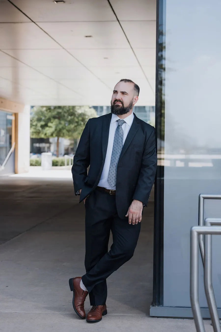 Travis McBride leaning against a glass wall in a suit